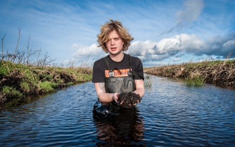 Filip stands in the water holding mud
