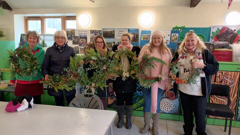 A group of 6 women inside the classroom showing their willow wreathes they have made from leaves and decorations