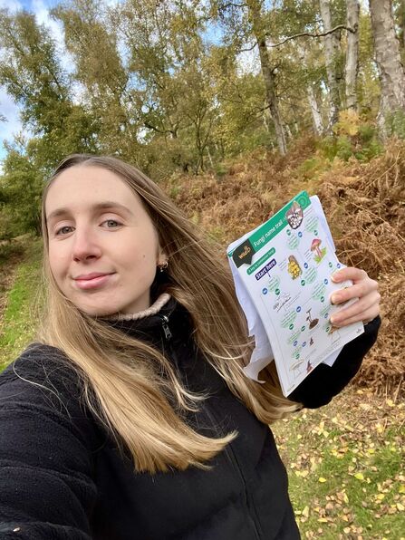 Trainee Ellen poses in a wooded nature reserve, holding an ID guide