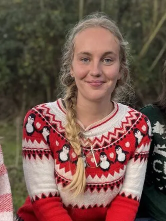 Trainee Katie smiles, wearing a red and white christmas jumper in a nordic style with penguins.